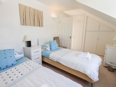 A bedroom with two single beds blue pillows and polka dot bedding a white nightstand a brown chair and built in cupboards at Fell Sweep in Keswick