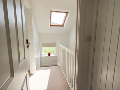 A stair landing with a skylight window a small window with a blind and a red decorative object on the windowsill at Fell Sweep in Keswick