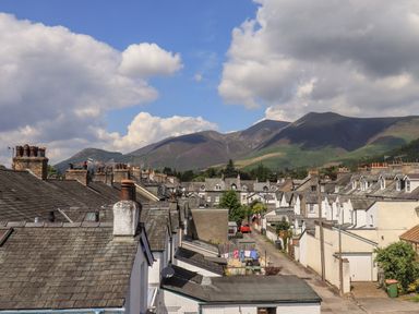 A residential area with rows of houses and chimneys in front of green hills and a partly cloudy sky at Fell Sweep in Keswick