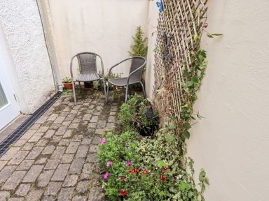 A small outdoor patio with two metal chairs potted plants and a trellis with climbing plants at Fell Sweep in Keswick
