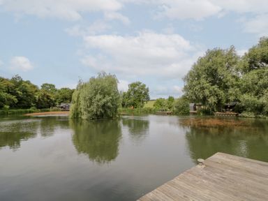 View of a lake with trees and fishing huts at Maple Lodge at Bridge Lake Farm &amp; Fishery, Chacombe