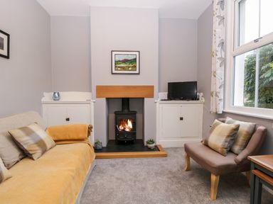 A living room with a fireplace between two white cabinets one holding a television and two sofas with cushions at 7 Railway Cottages in Newby Bridge