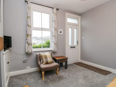 A corner of a room with a window and white door a beige armchair with cushions and two nested tables at 7 Railway Cottages in Newby Bridge