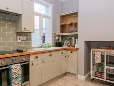 A kitchen with light cabinets a window above the sink and kitchen utensils at 7 Railway Cottages in Newby Bridge