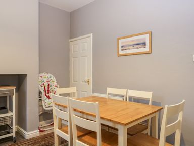 A dining room with a wooden table and six chairs a high chair in the corner and a framed picture on the wall at 7 Railway Cottages in Newby Bridge