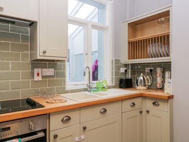 A kitchen with a sink under a window plates in a wall rack and kitchen appliances on wooden countertops at 7 Railway Cottages in Newby Bridge
