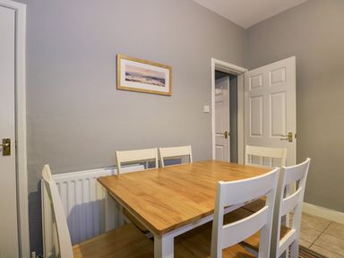 A dining area with a wooden table and white chairs next to a gray wall with a framed picture at 7 Railway Cottages in Newby Bridge