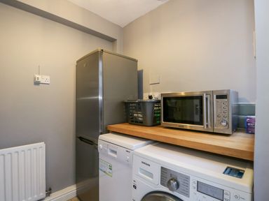 A utility room with a silver refrigerator dishwasher washing machine microwave and a basket on a wooden countertop at 7 Railway Cottages in Newby Bridge