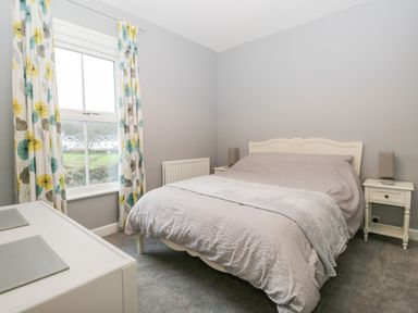 A bedroom with a bed between two nightstands and a window with floral curtains at 7 Railway Cottages in Newby Bridge
