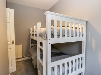 A small bedroom with white bunk beds and a partially open door at 7 Railway Cottages in Newby Bridge