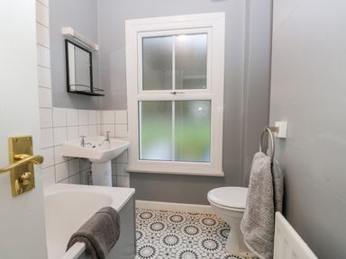 A bathroom with a bathtub a sink a toilet a towel ring and patterned floor at 7 Railway Cottages in Newby Bridge