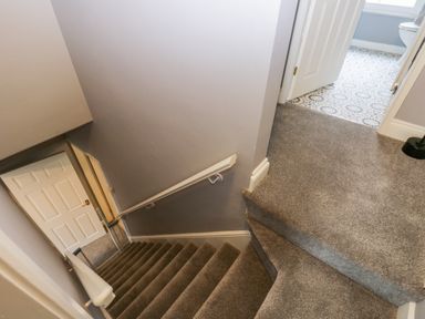 A carpeted staircase leading down to a closed door with a white handrail in a hallway at 7 Railway Cottages in Newby Bridge