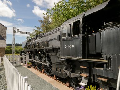 A black steam locomotive next to a white picket fence and a railway signal at 7 Railway Cottages in Newby Bridge