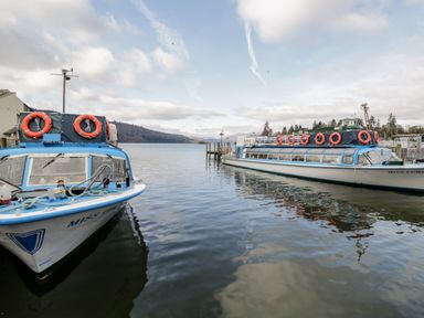 Two passenger boats docked on a lake with hills and partly cloudy sky in the background at 7 Railway Cottages in Newby Bridge
