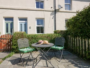 A small outdoor patio with two chairs and a round metal table with hats on it at 7 Railway Cottages in Newby Bridge
