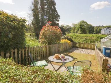 A small garden with a round metal table and two chairs surrounded by a wooden fence at 7 Railway Cottages in Newby Bridge