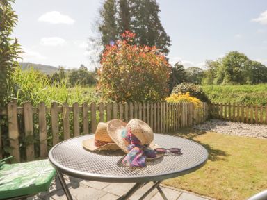 A garden patio with a round metal table holding two straw hats and sunglasses at 7 Railway Cottages in Newby Bridge