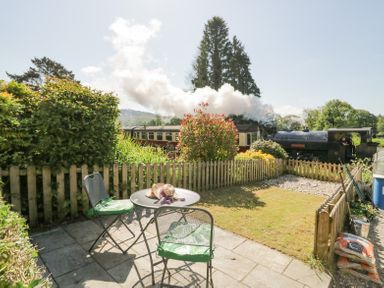 A small garden with patio furniture and a steam train passing behind a wooden fence at 7 Railway Cottages in Newby Bridge