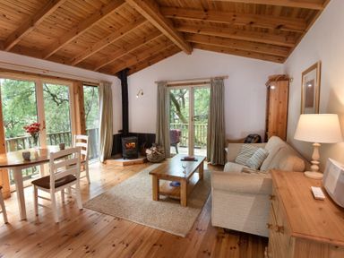 A living room with a wooden ceiling a wood stove a sofa a coffee table and a dining table with chairs at Chapel House in Torridon