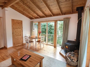 A room with wooden ceiling and floor a table with three chairs a wood stove and a basket of firewood at Chapel House in Torridon