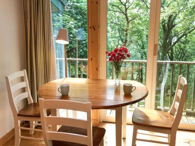 A dining table with two cups and a vase of flowers near sliding glass doors with a view of trees at Chapel House in Torridon
