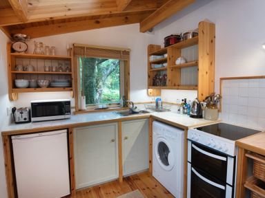 A kitchen with wooden shelves a washing machine a microwave and a stove next to a window at Chapel House in Torridon