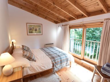 A bedroom with a bed a lamp and a window showing trees outside at Chapel House in Torridon