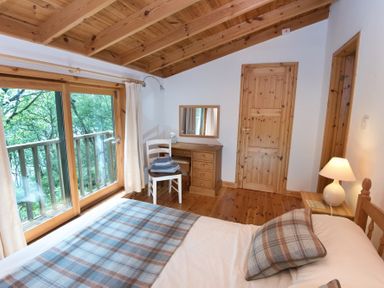 A bedroom with a wooden ceiling a bed with plaid bedding a chair with folded towels and a desk with a mirror at Chapel House in Torridon