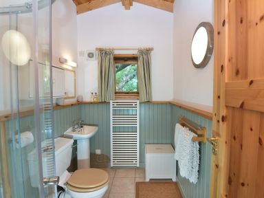 A bathroom with a toilet, sink, shower, towel rack, window with curtains, and wooden door at Chapel House in Torridon