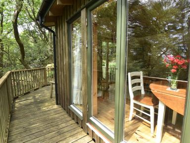 A wooden balcony outside a cabin with a table and chair visible through large windows at Chapel House in Torridon