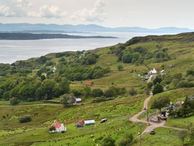 A rural area with green hills trees houses and a road by a large body of water at Chapel House in Torridon