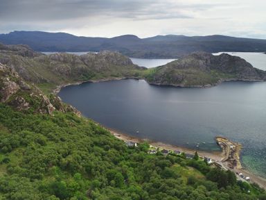 A coastal landscape with hills trees a small pier and houses by the water at Chapel House in Torridon