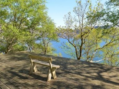 A wooden bench on a wooden deck overlooking trees and a body of water at Chapel House in Torridon