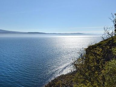 A body of water with a rocky shore and trees on the right and hills in the distance at Chapel House in Torridon