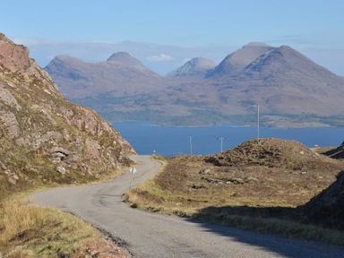 A winding road between hills with a body of water and mountains in the background at Chapel House in Torridon