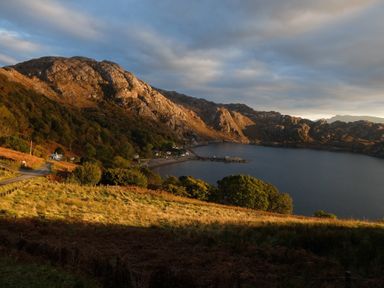 A coastal landscape with a road and houses near a body of water surrounded by rocky hills