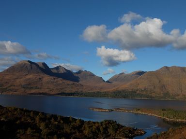 A body of water surrounded by trees and mountains under a blue sky at Chapel House in Torridon