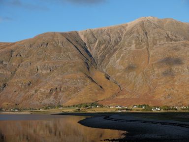 A mountain landscape with a body of water and houses at the base at Chapel House in Torridon