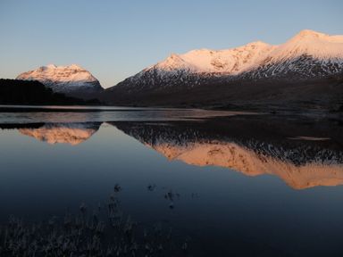Snow-capped mountains reflected in a lake at Chapel House in Torridon