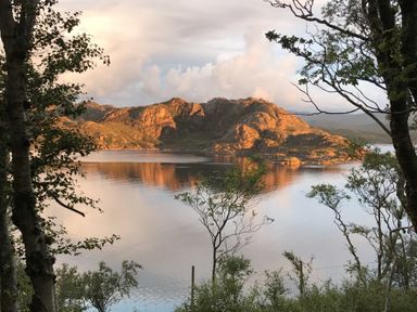 A lake with rocky hills in the background and trees in the foreground at Chapel House in Torridon