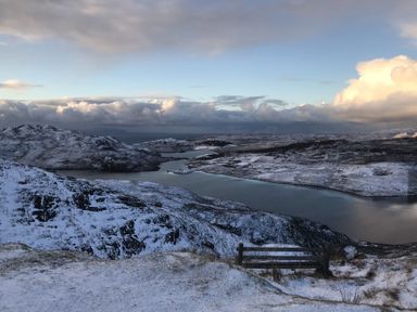 A snowy hillside overlooking a lake with mountains in the distance at Chapel House in Torridon