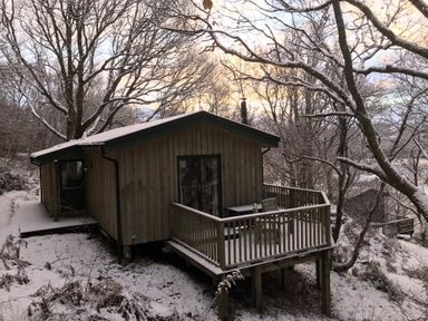 A wooden cabin with a deck and two chairs in a snowy forest at Chapel House in Torridon