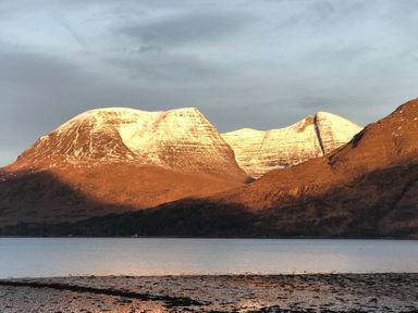 A mountain range with snow on the peaks near a body of water at Chapel House in Torridon