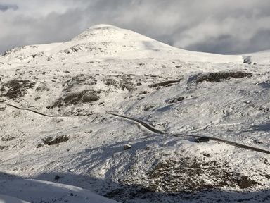 A snow-covered mountain with a winding road and a vehicle on the road at Chapel House in Torridon