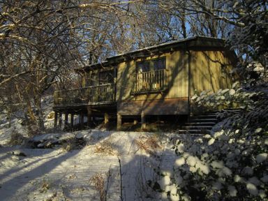 A wooden cabin on stilts surrounded by snow and leafless trees
