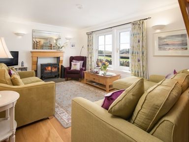 A living room with green sofas a wooden coffee table a fireplace and windows with curtains at Ardlarach Lodge Cullipool Isle Of Luing