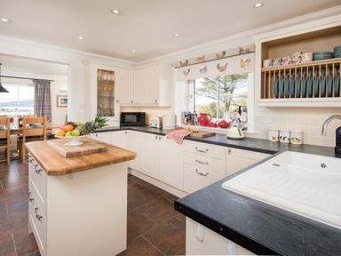 A kitchen with white cabinets black countertops a wooden island fruit bowl and a window with a roller blind with chicken patterns at Ardlarach Lodge Cullipool Isle Of Luing