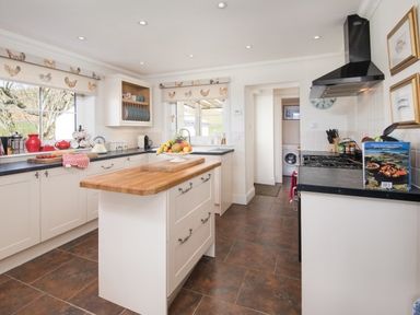 A kitchen with white cabinets a wooden island a stove and windows with chicken patterned blinds at Ardlarach Lodge in Cullipool Isle Of Luing