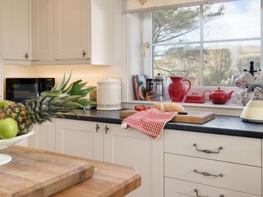 A kitchen counter with a cutting board holding bread and tomatoes next to a window with red teapots and a coffee press at Ardlarach Lodge in Cullipool Isle Of Luing