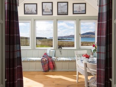 A dining room with a window seat overlooking countryside and water at Ardlarach Lodge in Cullipool Isle Of Luing